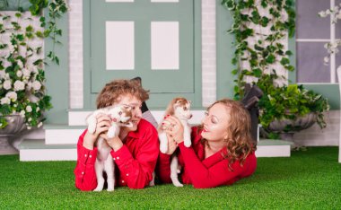 Mutlu anne ve oğul yeşil çimlerin üzerinde iki şirin köpek yavrusuyla poz veriyorlar.