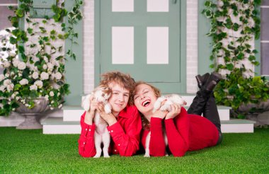 Mutlu anne ve oğul yeşil çimlerin üzerinde iki şirin köpek yavrusuyla poz veriyorlar.