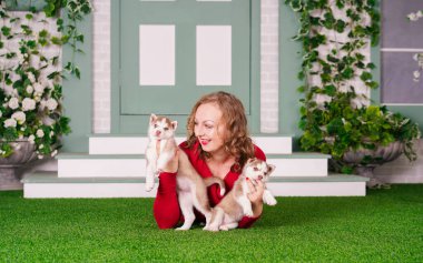 Güzel, beyaz, iri yarı, kırmızı kazaklı, yeşil çimenli, iri yapılı iki yavru köpeği olan bir kadın.