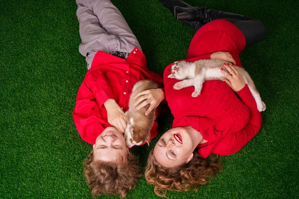 Bonne maman et son fils posent sur l'herbe verte avec deux petits chiots husky mignons — Photo