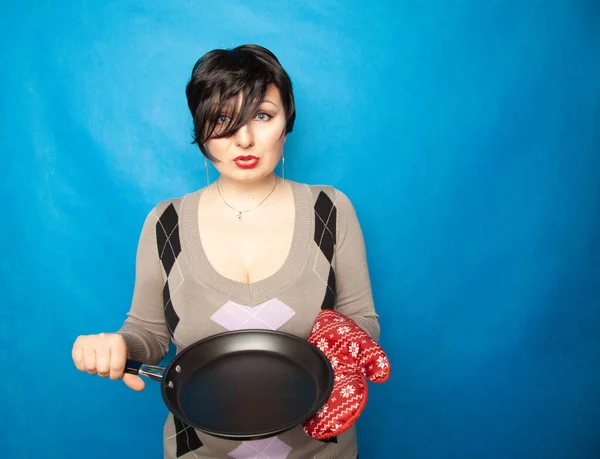 Chica con el pelo corto se para en un suéter con un gran guante de cocina rojo y una sartén vacía, listo para cocinar — Foto de Stock