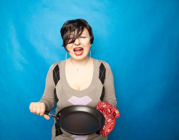 Девушка с короткими волосами стоит в свитере с большой красной кухонной перчаткой и пустой сковородкой, готовой к приготовлению — стоковое фото