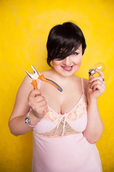 Bonito engraçado menina em lingerie fica com alicate e uma lâmpada e não sabe o que fazer com eles, como fazer reparos — Fotografia de Stock