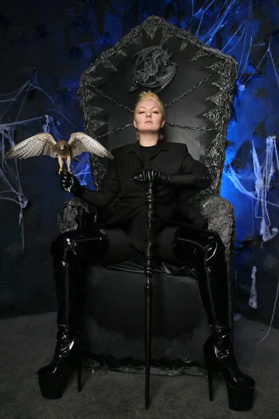 Photo of a female witch queen holding bird and sitting on a gothic scary black throne — Stock Photo, Image