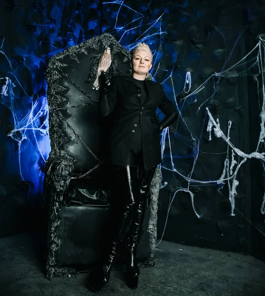 Фото королевы ведьм, держащей птицу и сидящей на готическом страшном черном троне — стоковое фото