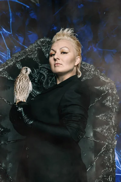 Photo of a female witch queen holding bird and sitting on a gothic scary black throne — Stock Photo, Image