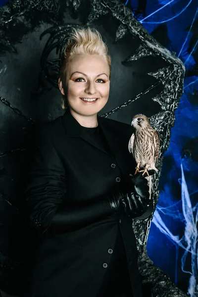 Photo of a female witch queen holding bird and sitting on a gothic scary black throne — Stock Photo, Image