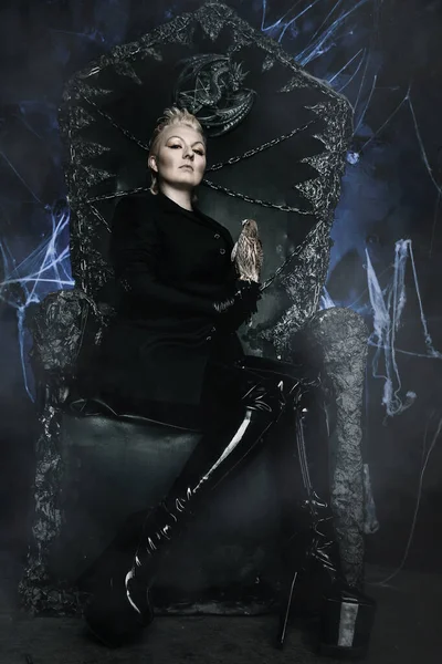 Foto einer weiblichen Hexenkönigin mit Vogel und auf einem gotischen beängstigenden schwarzen Thron sitzend — Stockfoto