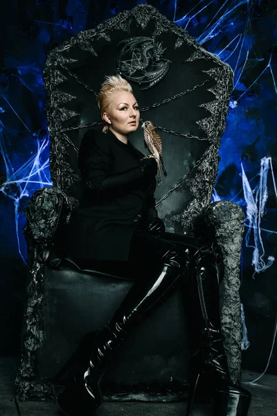女性魔女の女王が鳥を抱いてゴシック様式の恐ろしい黒い玉座に座っている写真 — ストック写真