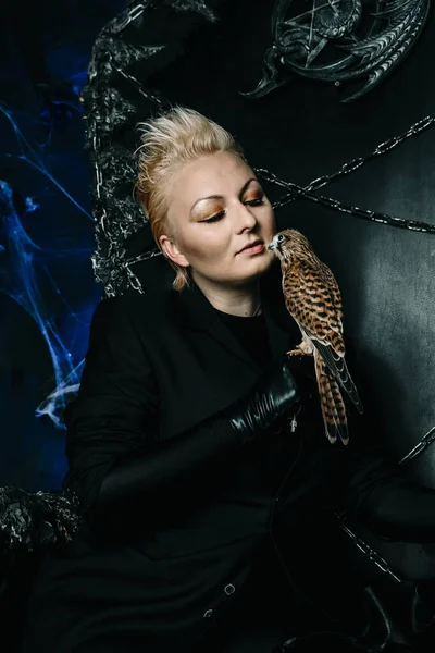 Photo of a female witch queen holding bird and sitting on a gothic scary black throne — Stock Photo, Image