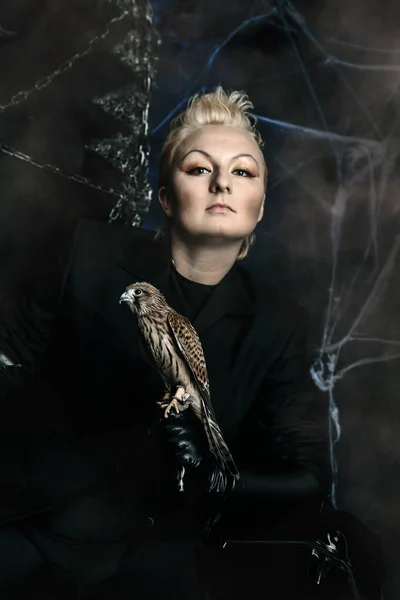 Photo of a female witch queen holding bird and sitting on a gothic scary black throne — Stock Photo, Image