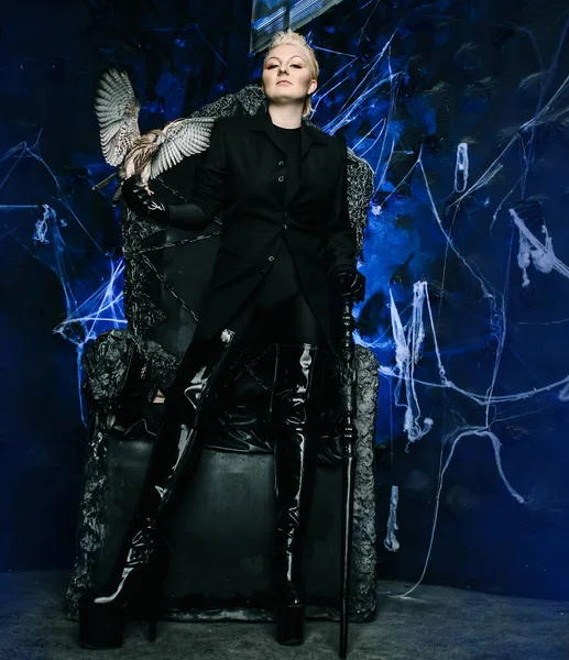 Photo of a female witch queen holding bird and sitting on a gothic scary black throne — Stock Photo, Image