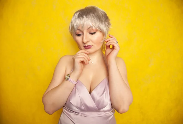 Happy short hair blond girl with plus size body posing in lilac color dress on yellow studio background — Stock Photo, Image