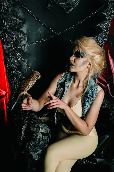 Fashionable halloween model with bird sitting on the big black throne alone in the scary night — Stock Photo, Image