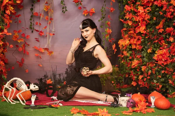 Chica de halloween de moda delgada con pelo negro en encaje gótico pin up vestido posando en el fondo de otoño con hojas de otoño —  Fotos de Stock