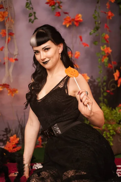 Chica de halloween de moda delgada con pelo negro en encaje gótico pin up vestido posando en el fondo de otoño con hojas de otoño —  Fotos de Stock