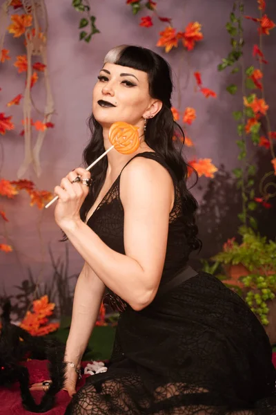 Slim moda halloween menina com cabelo preto em renda gótico pin up vestido posando no fundo do outono com folhas de outono — Fotografia de Stock