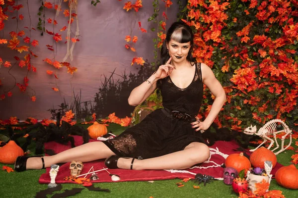 Chica de halloween de moda delgada con pelo negro en encaje gótico pin up vestido posando en el fondo de otoño con hojas de otoño —  Fotos de Stock