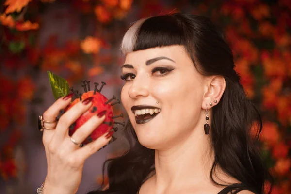 Красива дівчина на Хеллоуїн в чорному одязі з мертвим червоним яблуком в руці на фоні осіннього листя — стокове фото