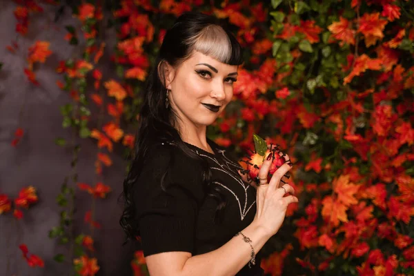 Krásná halloween dívka v černé pin up oblečení s mrtvým červeným jablkem v ruce na podzim opustí pozadí sám — Stock fotografie
