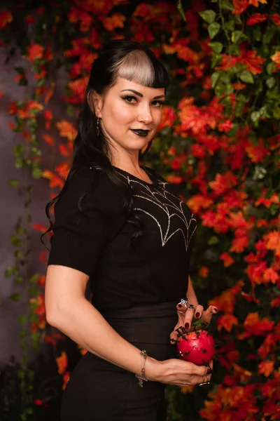 Bela menina halloween em preto pin up roupas com maçã vermelha morta na mão no outono folhas fundo sozinho — Fotografia de Stock