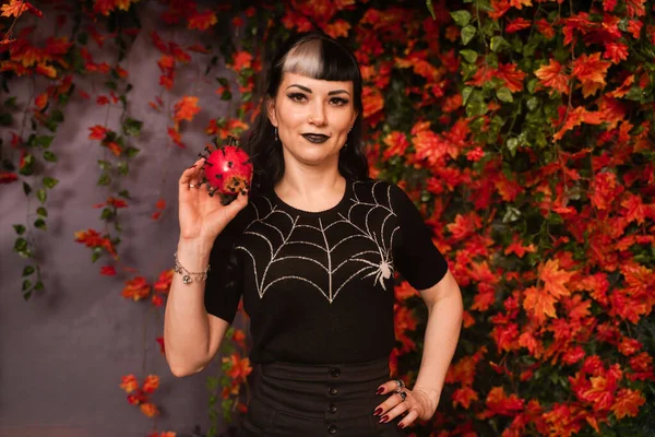 Bella ragazza di Halloween in nero pin up vestiti con mela rossa morta in mano su autunno lascia sfondo da solo — Foto Stock