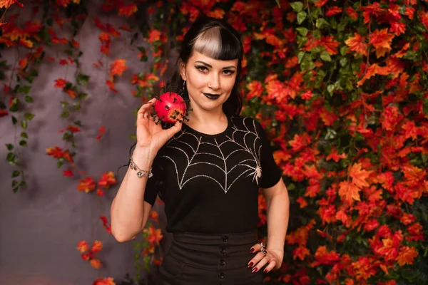 Bella ragazza di Halloween in nero pin up vestiti con mela rossa morta in mano su autunno lascia sfondo da solo — Foto Stock