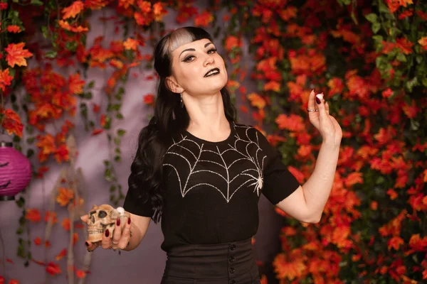 Feliz jovem mulher de cabelo preto segurando e comendo doces de olhos de chocolate de scull. Estúdio retrato sobre outono folhas fundo — Fotografia de Stock