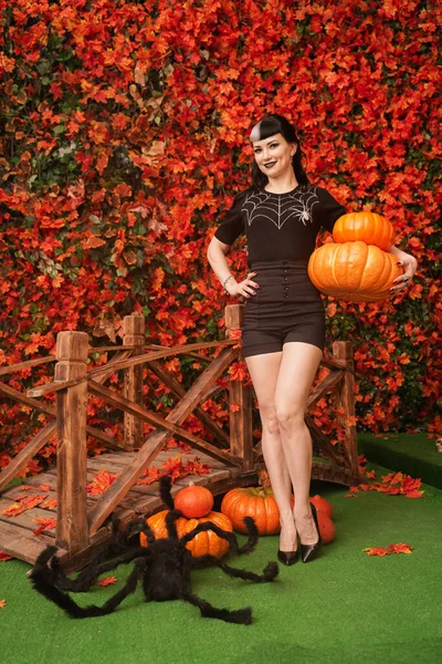 Sexy e atraente bruxa morena no outono colorido parque com laranja e folhas vermelhas posando com abóboras — Fotografia de Stock