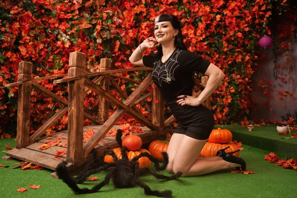 Sexy y atractiva bruja morena en otoño colorido parque con hojas naranjas y rojas posando con calabazas —  Fotos de Stock