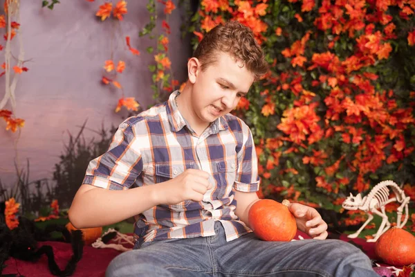 Foto de un joven enojado en Halloween con camisa a cuadros clásica sosteniendo calabaza naranja sobre el fondo de la calle con hojas de otoño —  Fotos de Stock