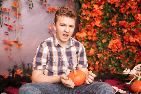 Foto de un joven enojado en Halloween con camisa a cuadros clásica sosteniendo calabaza naranja sobre el fondo de la calle con hojas de otoño —  Fotos de Stock