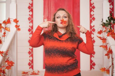 Artı turuncu kazaklı beyaz kız elinde sonbahar kırmızı akçaağaç yaprağı tutarken yüzü kapalıydı. Yetişkin bir kız beyaz evinin verandasında duruyor..