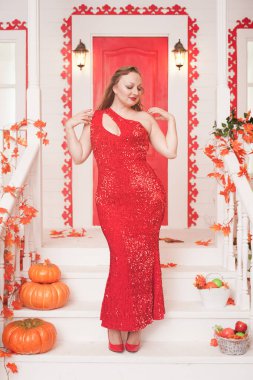 Beyaz sarayının verandasında kırmızı maksi elbise giyen genç ve şık tombul bir kadın. Sonbahar modası, zarif görünüş. Artı boyut modeli.