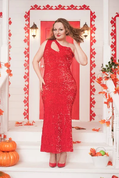 Joven mujer gordita con estilo vistiendo maxi vestido rojo en el porche de su casa blanca. Moda de otoño, aspecto elegante. Modelo de tamaño más . — Foto de Stock
