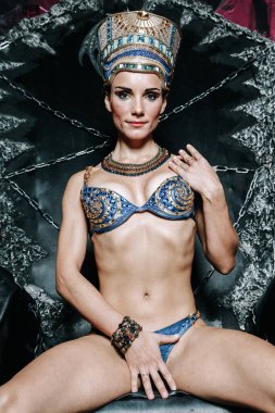 Stüdyonun arka planında mavi mayo giymiş, kocaman altın başlıklı, güzel, zayıf Mısırlı kadın.