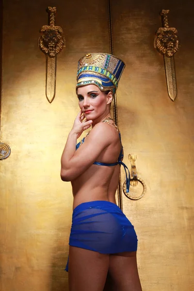 Mulher egípcia fina bonita com maçãs do rosto pronunciadas em uma enorme cobertura para a cabeça de ouro sem cabelo em um maiô azul no fundo no estúdio — Fotografia de Stock