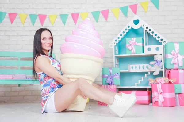 Mooie fitness meisje in witte shorts en stijlvolle korte jurk poseren met enorme kunstmatige voedsel desserts op de achtergrond van de kamer. Charmante vrolijke slanke vrouw spelen met voedsel tijdens het dieet. — Stockfoto