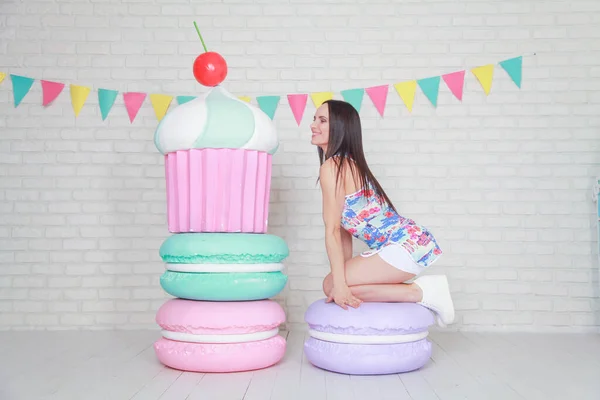 Mooie fitness meisje in witte shorts en stijlvolle korte jurk poseren met enorme kunstmatige voedsel desserts op de achtergrond van de kamer. Charmante vrolijke slanke vrouw spelen met voedsel tijdens het dieet. — Stockfoto