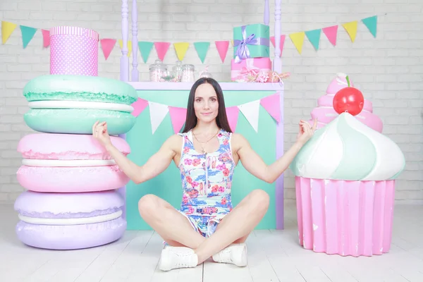 Mooie fitness meisje in witte shorts en stijlvolle korte jurk poseren met enorme kunstmatige voedsel desserts op de achtergrond van de kamer. Charmante vrolijke slanke vrouw spelen met voedsel tijdens het dieet. — Stockfoto