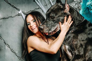 Küçük siyah elbiseli güzel, zayıf bir kadın. Büyük Danimarkalı köpeğiyle birlikte Cadılar Bayramı 'nın arka planında büyük, korkunç siyah tahtta poz veriyor.