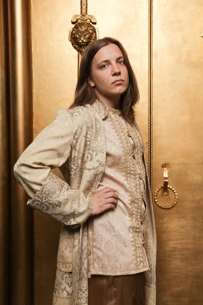 charming shy young teen guy in a medieval style gold suit in a photo Studio is ready to go to a party