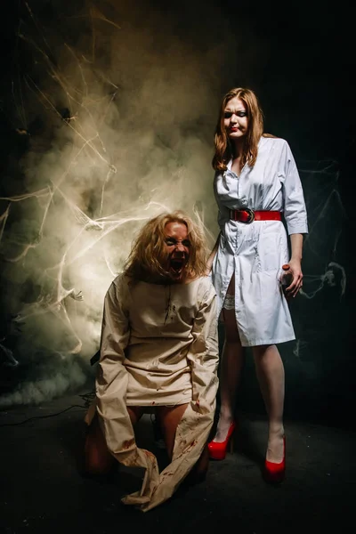 Par sexy de médico e paciente na festa de Halloween. uma menina bonita em meias e um roupão de enfermeiras e um cara em uma camisa de força com sangue de sua boca . — Fotografia de Stock