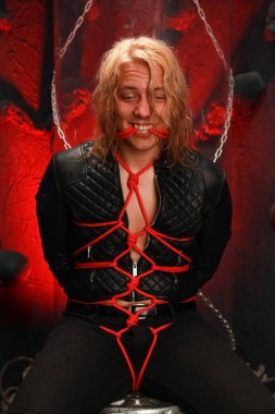 Yakışıklı, uzun saçlı, deri ceketli ve kırmızı iplerle bağlanmış bir adam. Seksi kölelik memeleri bdsm ve egemen olmak