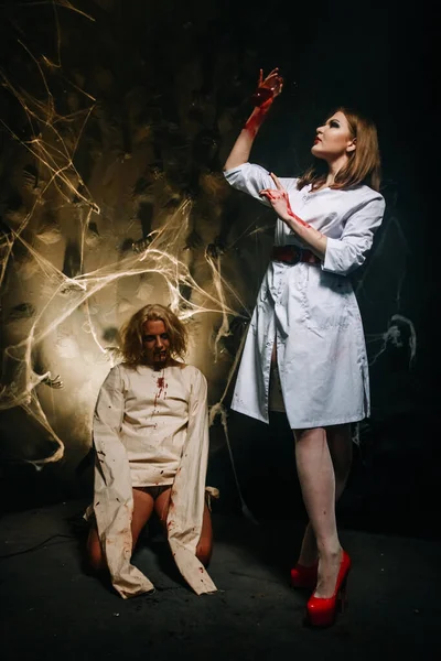 Par sexy de médico e paciente na festa de Halloween. uma menina bonita em meias e um roupão de enfermeiras e um cara em uma camisa de força com sangue de sua boca . — Fotografia de Stock