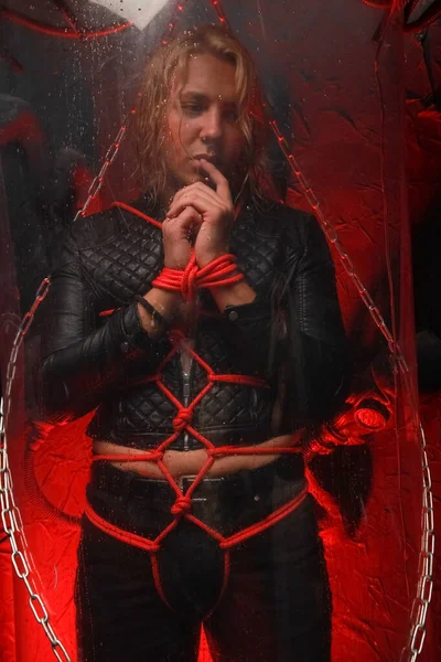 Sexual sweet blond male captive is tied up with red ropes and stands in a transparent space tube ready for a sex party as slave — Stock Photo, Image