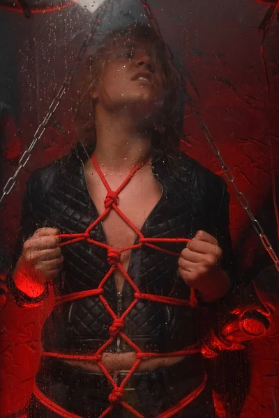Сексуальний солодкий блондинка чоловік в полоні зв'язаний червоними мотузками і стоїть в прозорій космічній трубці, готовій до секс-вечірки як раб — стокове фото