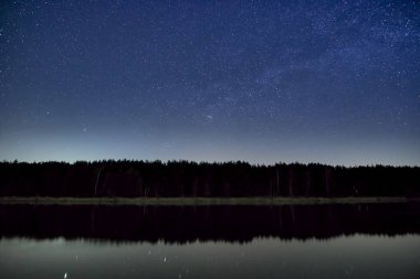 Şeffaf Nisan gecesi nehir ve orman üzerinde Samanyolu ile yıldız dolu harika güzel gece gökyüzü
