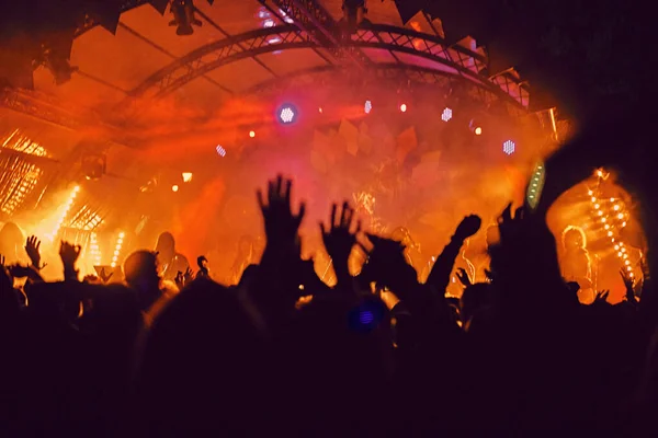 Abstract blur atmosphere: happy people enjoying outdoor music festival concert, raised up hands and clapping of pleasure, active night life concept, play of light and shadow on the huge stage