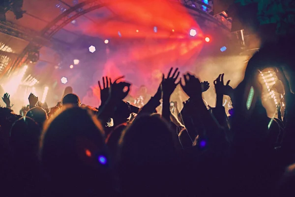 Abstract blur atmosphere: happy people enjoying outdoor music festival concert, raised up hands and clapping of pleasure, active night life concept, play of light and shadow on the huge stage